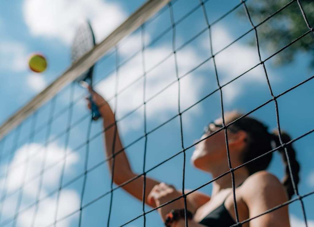 A girl hits a ball with a racket behind a portable tennis net