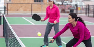 Two women wearing pink play pickleball on an outdoor court
